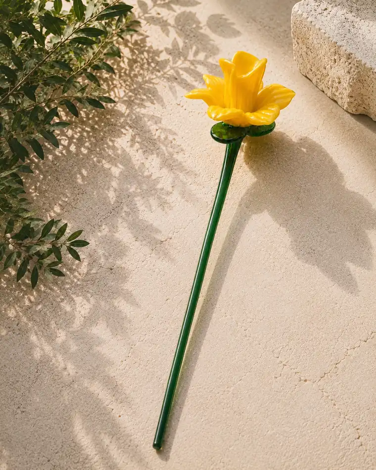 A yellow glass daffodil on a green glass stem, set on limestone paving.