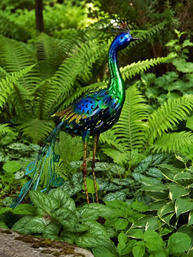 A metal peacock sculpture among ferns in daylight.