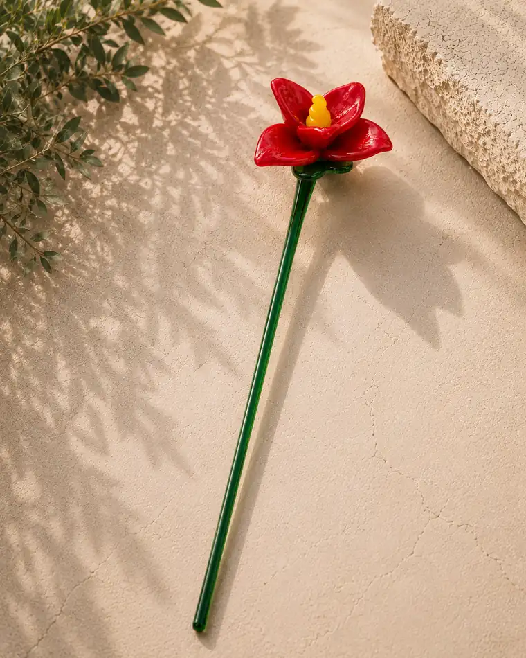 A red glass flower with a yellow centre, resting on limestone.